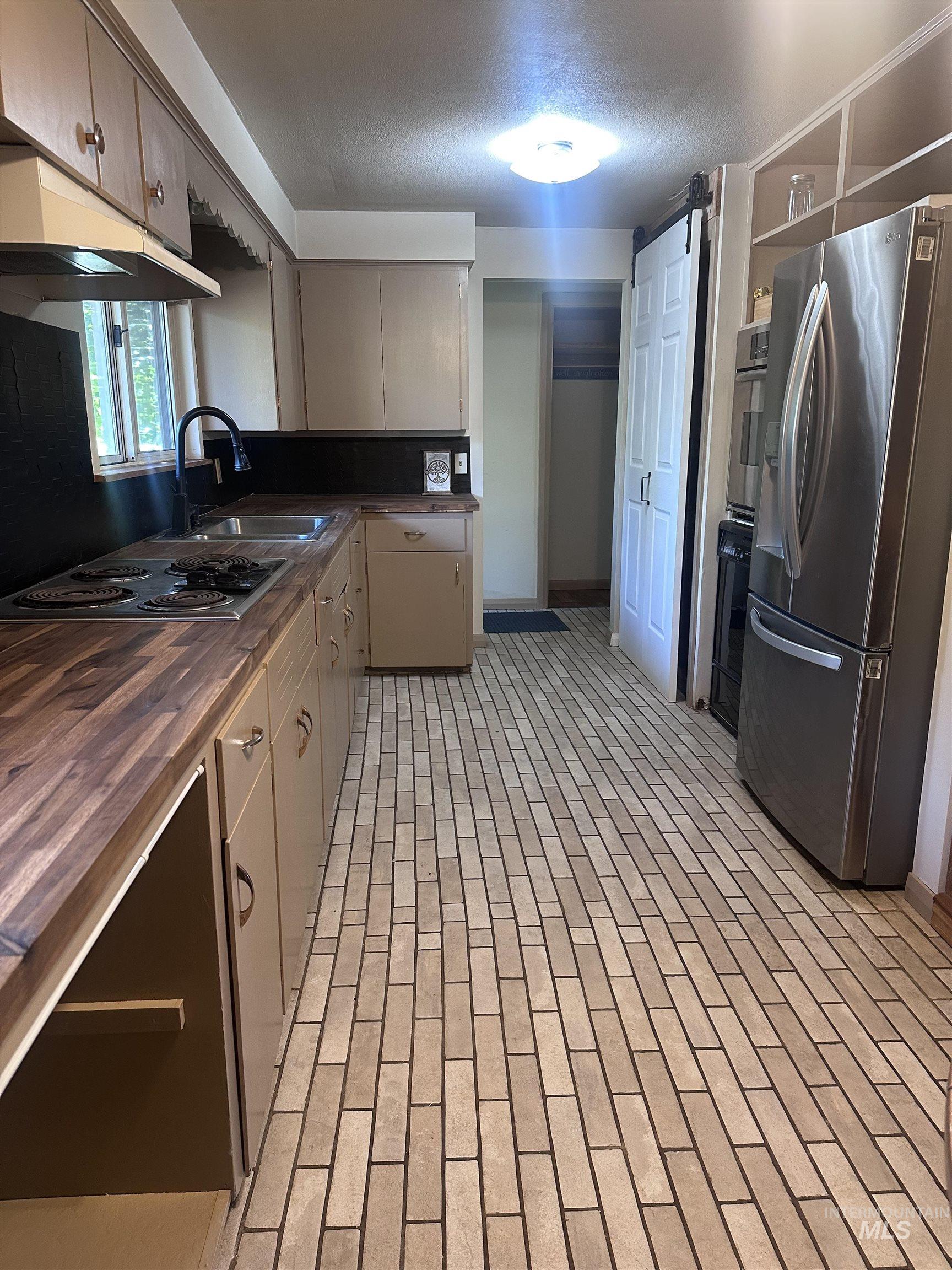 Kitchen featuring butcher block countertops, stainless steel appliances, brick patterned floors, under cabinet range hood, and open shelves