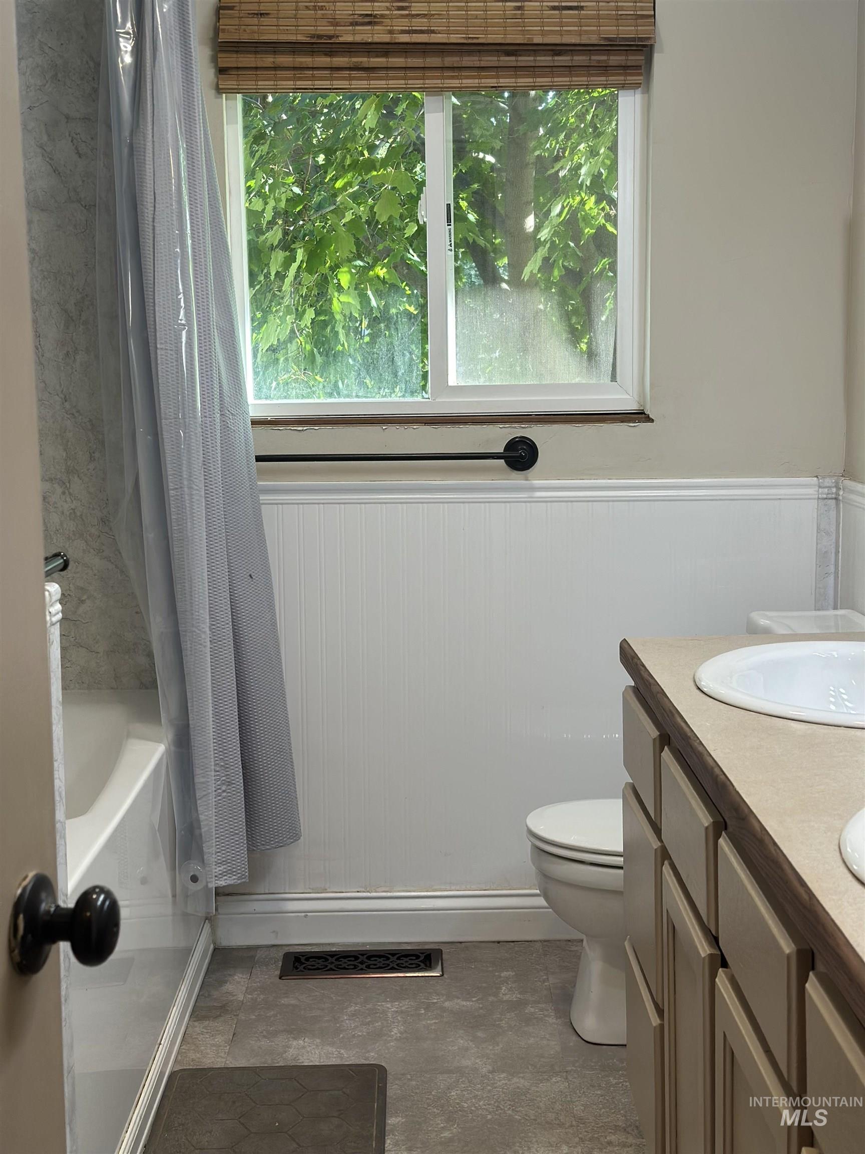 Full bath with a wainscoted wall, double vanity, and shower / tub combo with curtain