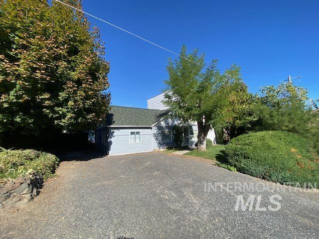 View of property hidden behind natural elements with gravel driveway