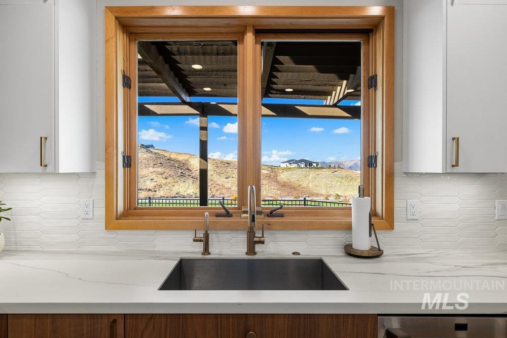 Kitchen view of tasteful backsplash, light stone countertops, white cabinets, and stainless steel dishwasher