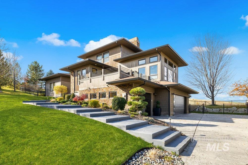 View of front of property with concrete driveway, a chimney, stone siding, a balcony, and an attached garage