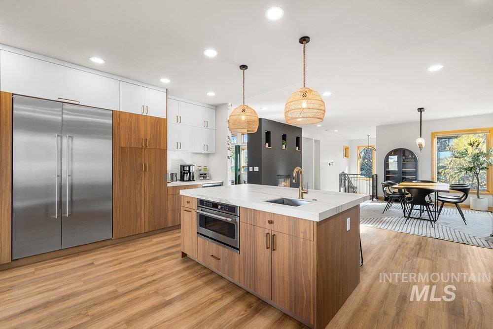 Kitchen featuring brown cabinets, modern cabinets, appliances with stainless steel finishes, light countertops, and pendant lighting