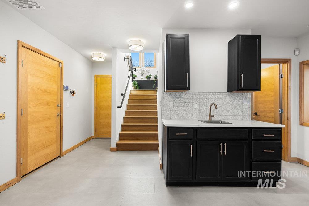 Bar area with dark cabinets, stairway, decorative backsplash, light stone counters, and recessed lighting
