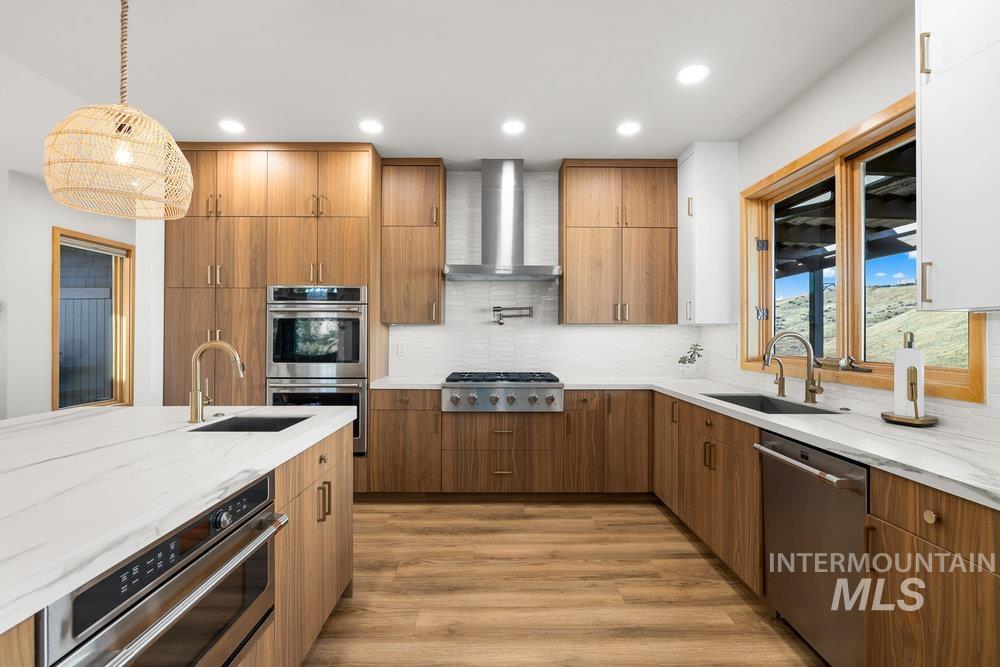 Kitchen featuring light stone counters, stainless steel appliances, light wood finished floors, wall chimney range hood, and tasteful backsplash