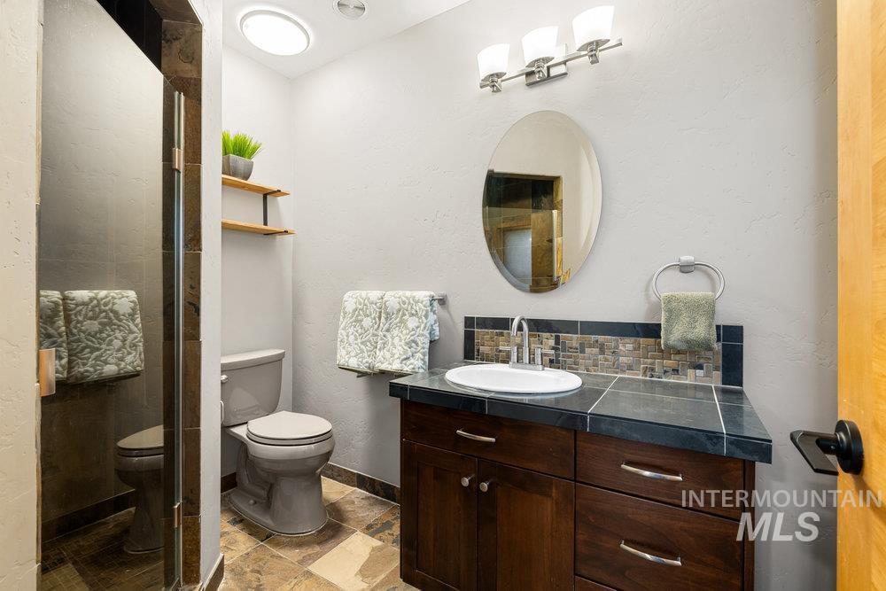 Full bath with a textured wall, vanity, a shower stall, backsplash, and light stone finish floors