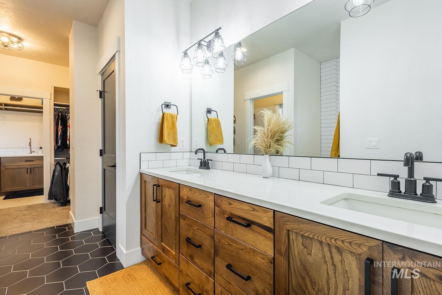 Bathroom with double vanity, a spacious closet, and dark tile patterned floors
