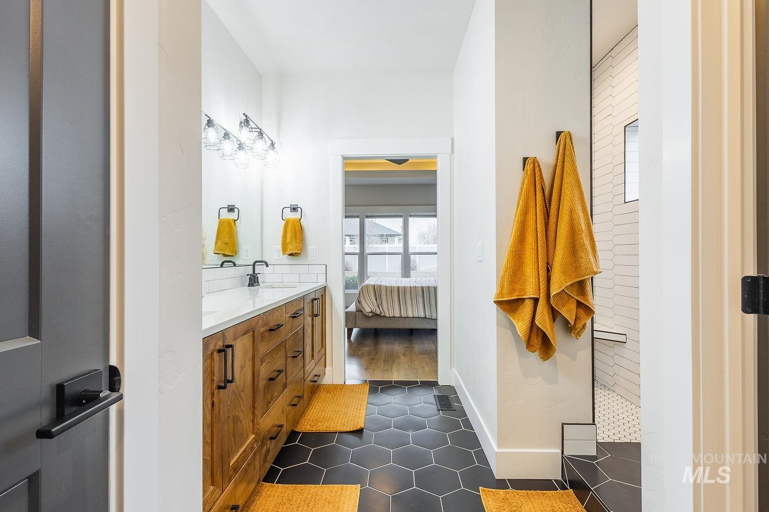 Ensuite bathroom with double vanity, walk in shower, and dark tile patterned flooring