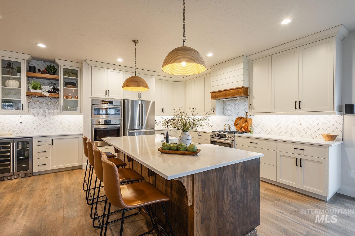 Kitchen with glass insert cabinets, wine cooler, a center island with sink, a kitchen breakfast bar, and decorative light fixtures