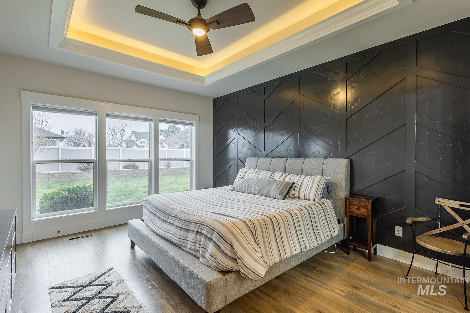 Bedroom with an accent wall, wood finished floors, ceiling fan, a tray ceiling, and a decorative wall