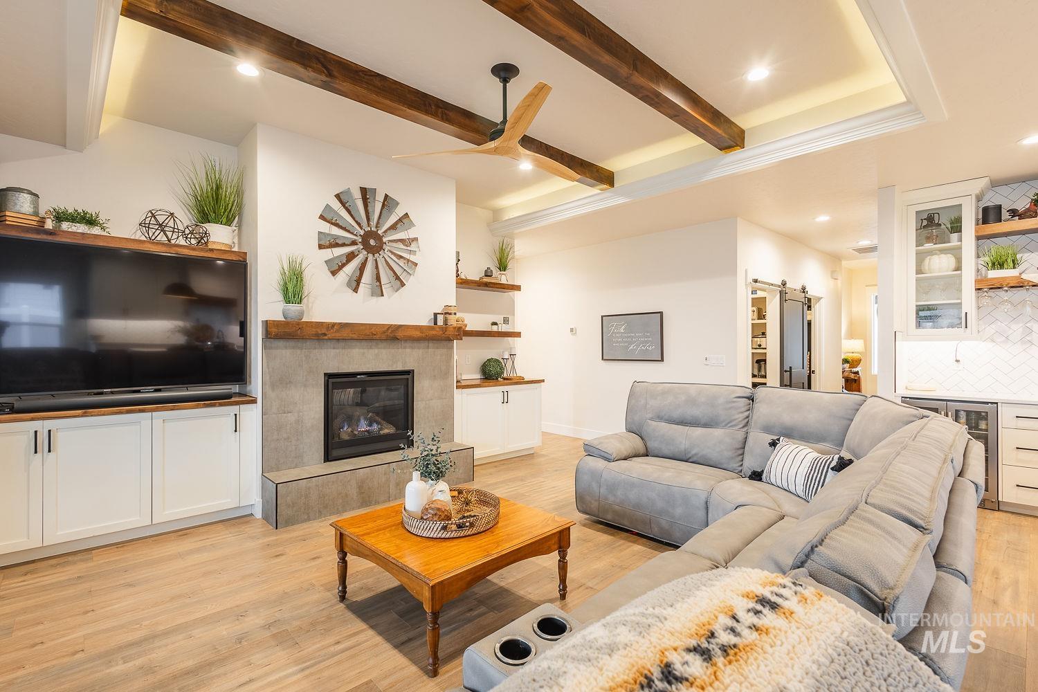 Living area featuring a barn door, light wood-type flooring, beamed ceiling, wine cooler, and a tile fireplace