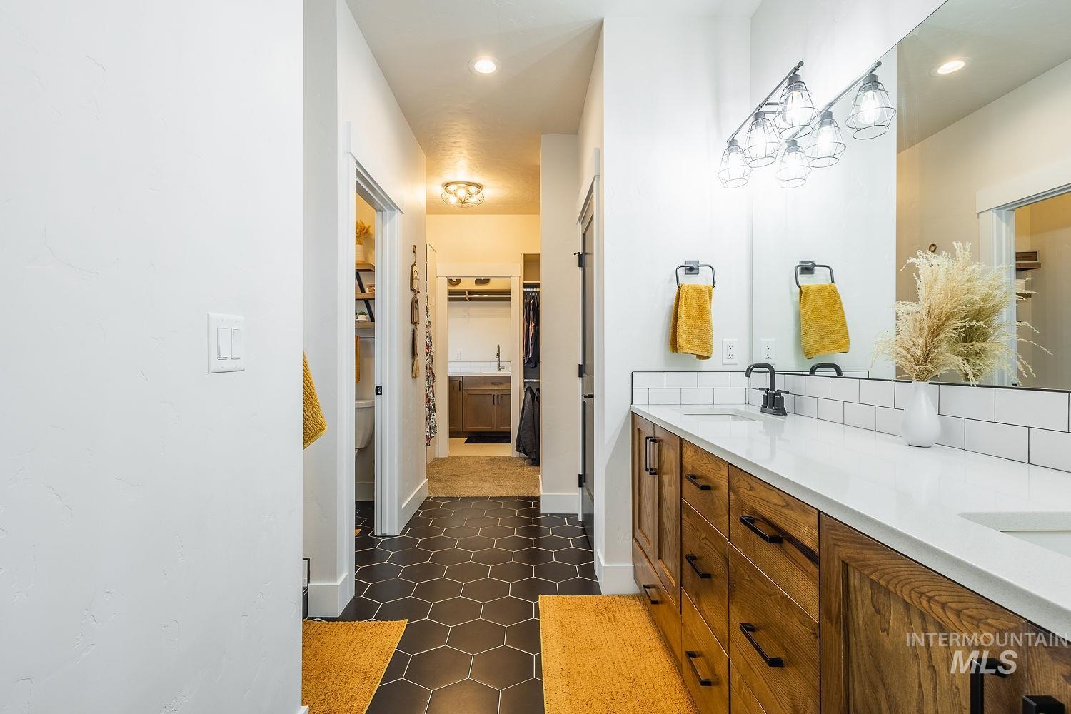 Full bathroom with a spacious closet, double vanity, dark tile patterned floors, and recessed lighting