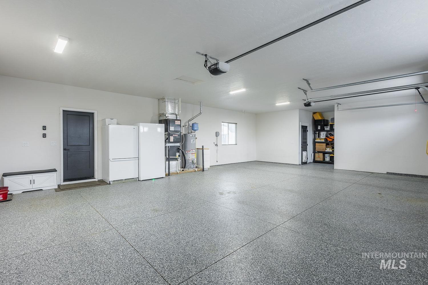 Garage featuring freestanding refrigerator, gas water heater, heating unit, and a garage door opener
