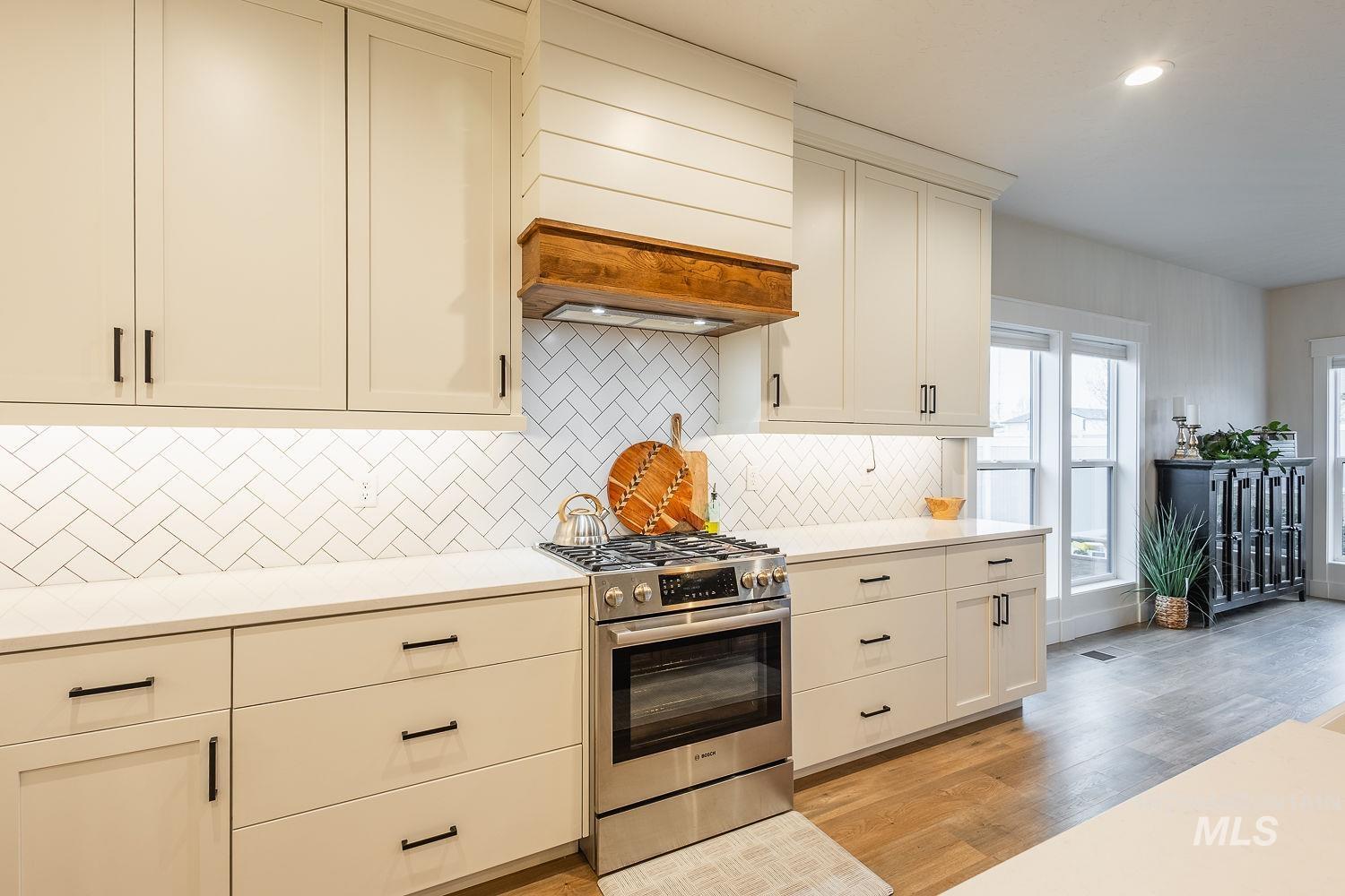 Kitchen featuring stainless steel gas range, premium range hood, light wood-type flooring, white cabinetry, and backsplash