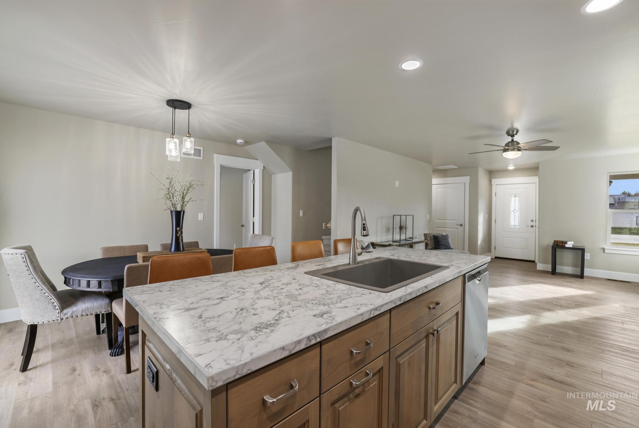 Kitchen with brown cabinets, light wood finished floors, pendant lighting, a center island with sink, and recessed lighting