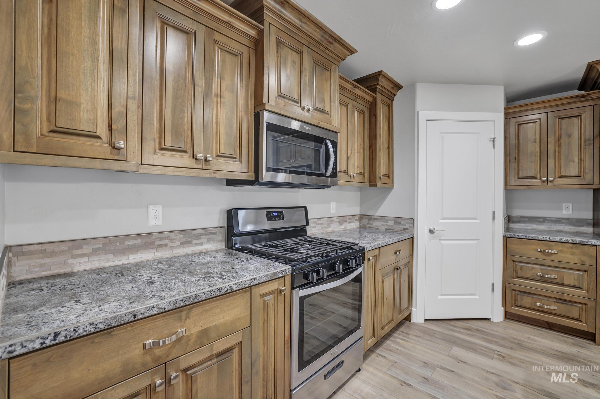 Kitchen with appliances with stainless steel finishes, brown cabinetry, light stone countertops, and recessed lighting