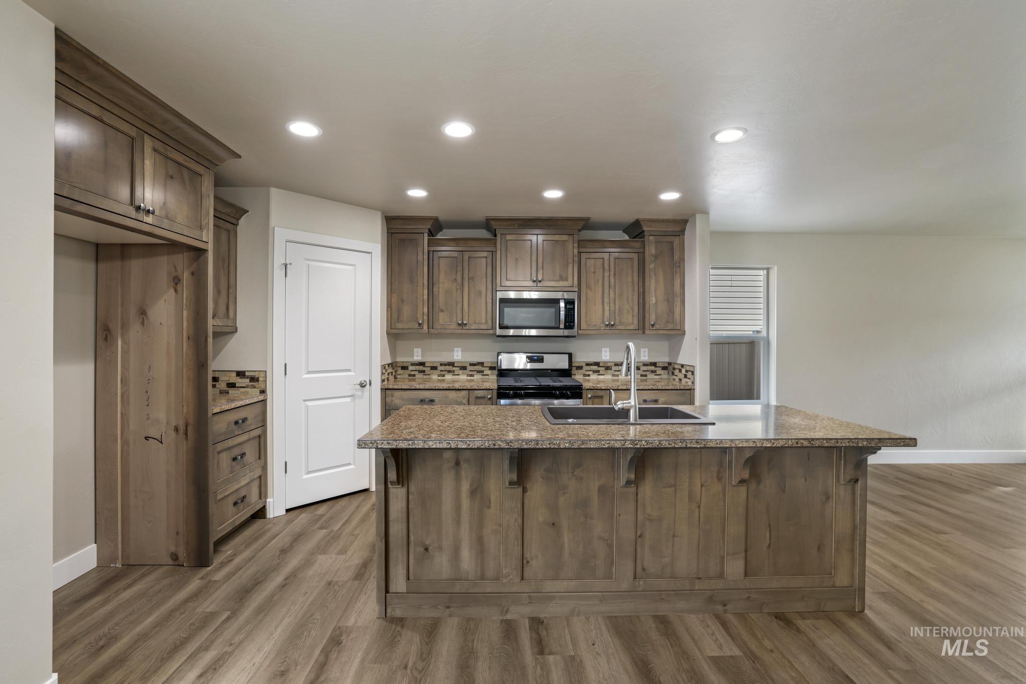 Kitchen featuring stainless steel appliances, an island with sink, a kitchen breakfast bar, recessed lighting, and dark stone countertops