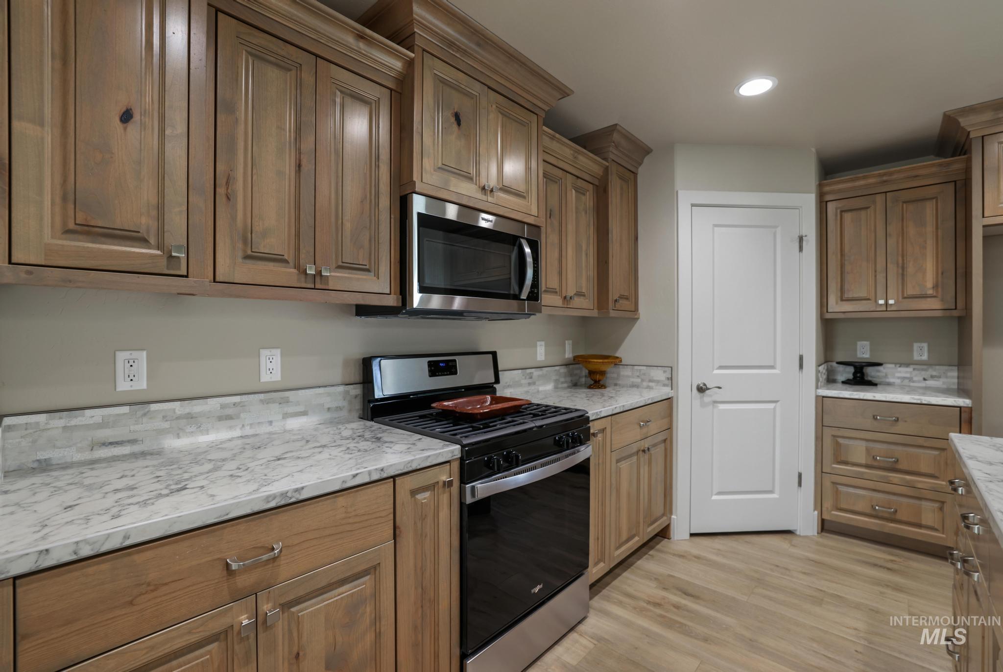 Kitchen featuring appliances with stainless steel finishes, light wood finished floors, recessed lighting, brown cabinetry, and light stone countertops