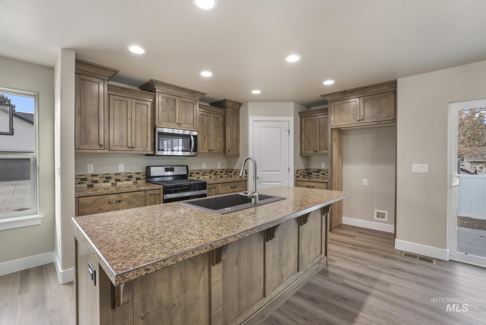 Kitchen featuring healthy amount of natural light, appliances with stainless steel finishes, a kitchen island with sink, recessed lighting, and a breakfast bar area
