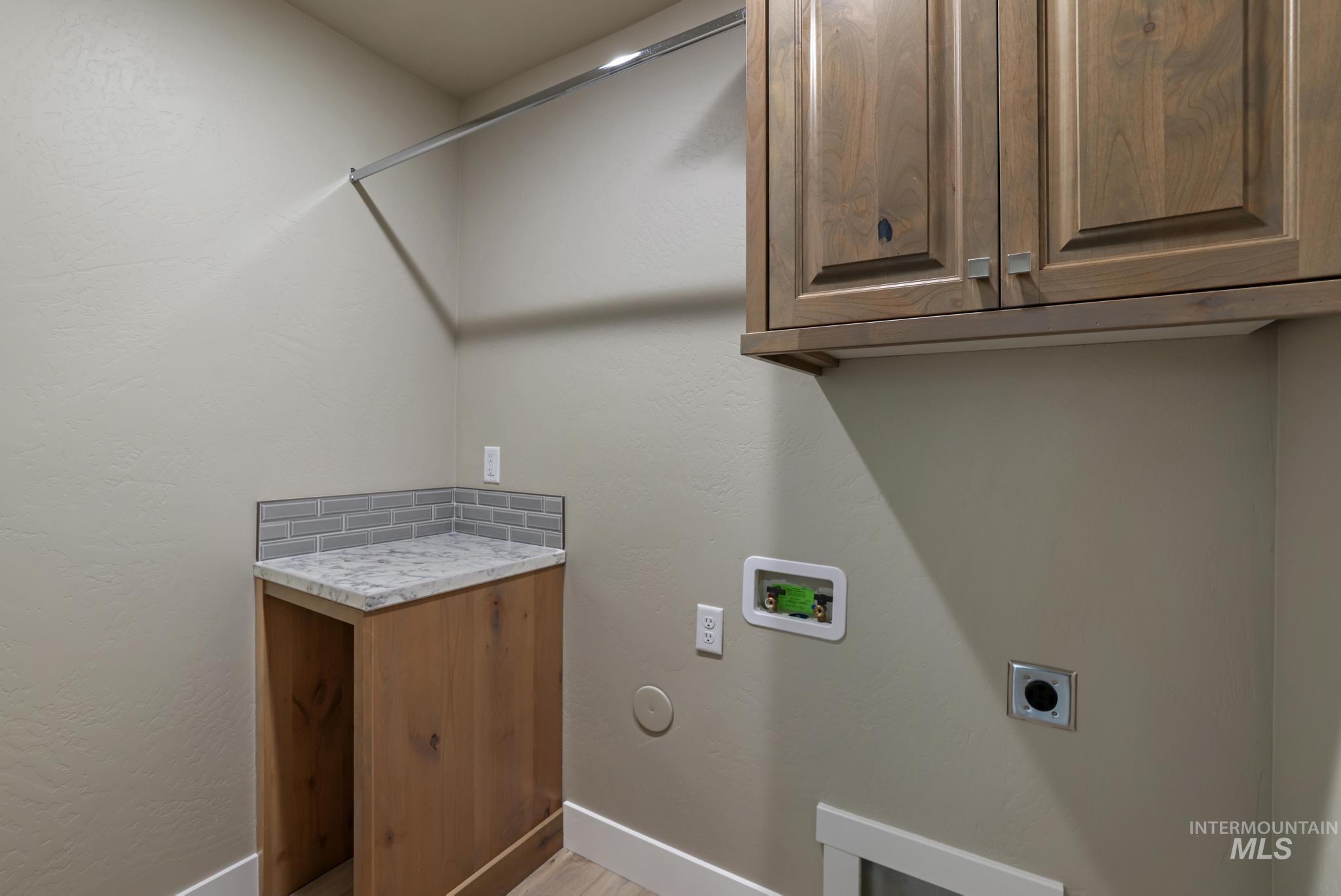 Laundry area featuring electric dryer hookup, a textured wall, cabinet space, and washer hookup