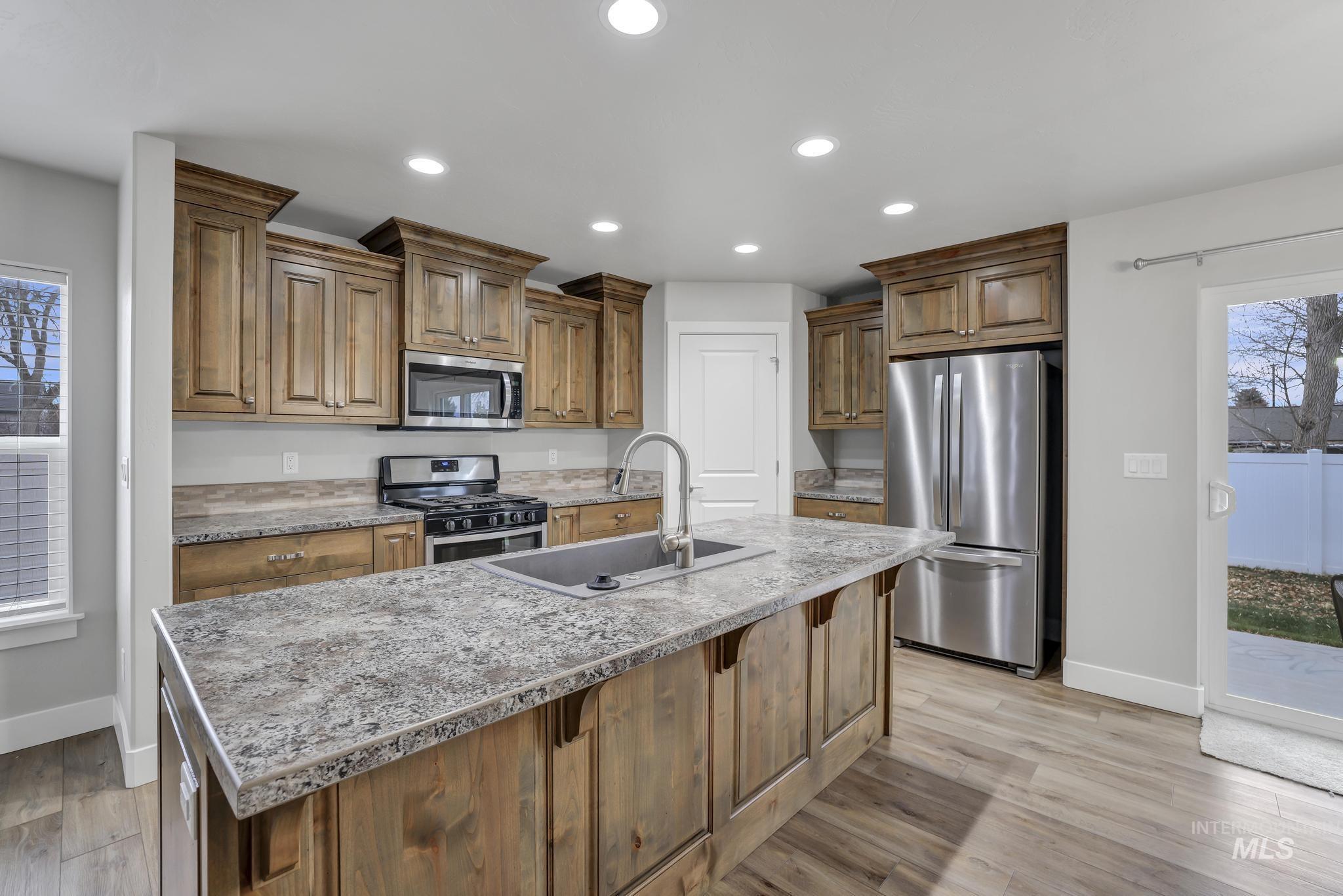 Kitchen with healthy amount of natural light, stainless steel appliances, recessed lighting, a kitchen island with sink, and light wood-style floors
