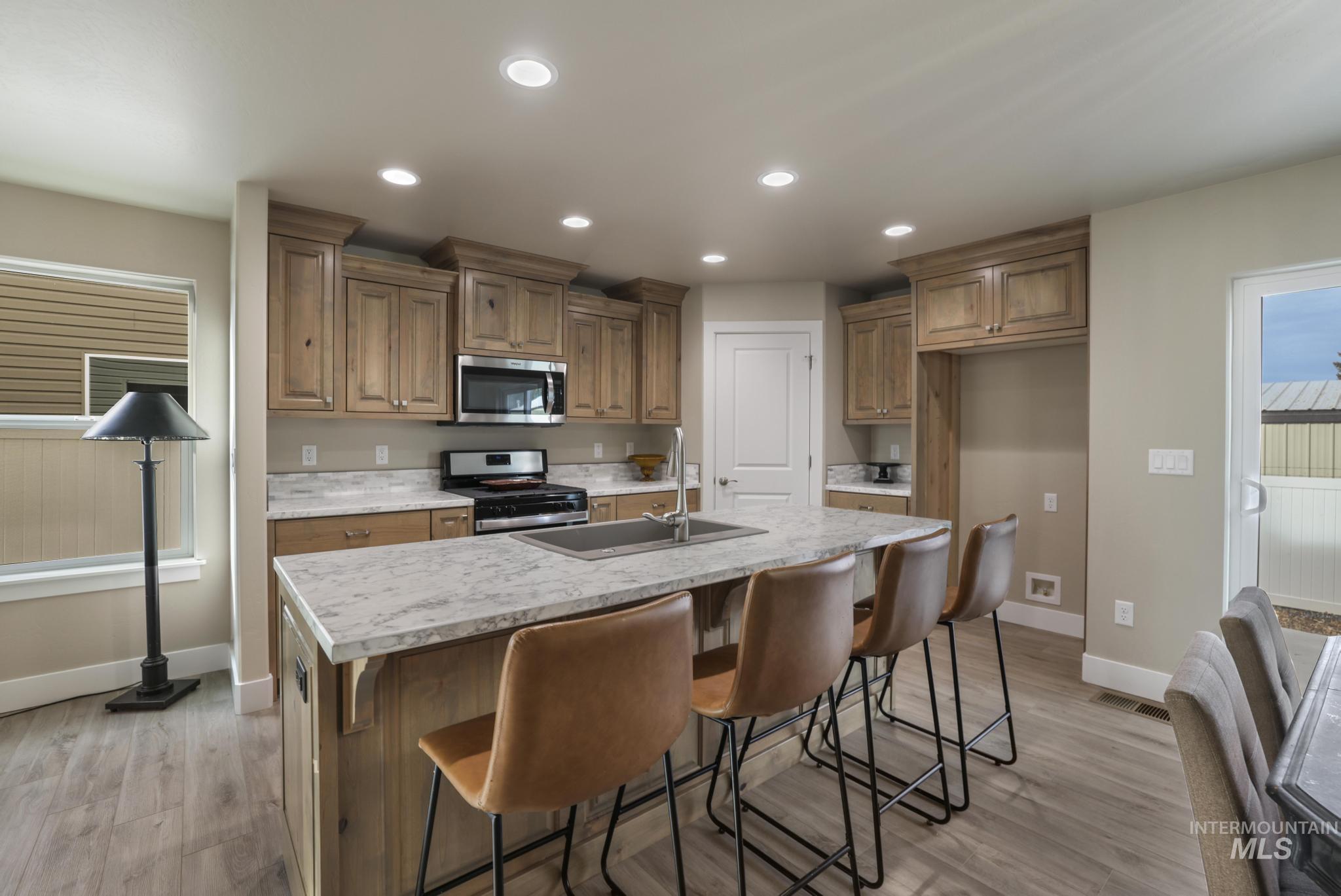 Kitchen featuring recessed lighting, stainless steel appliances, a breakfast bar, an island with sink, and light wood-type flooring
