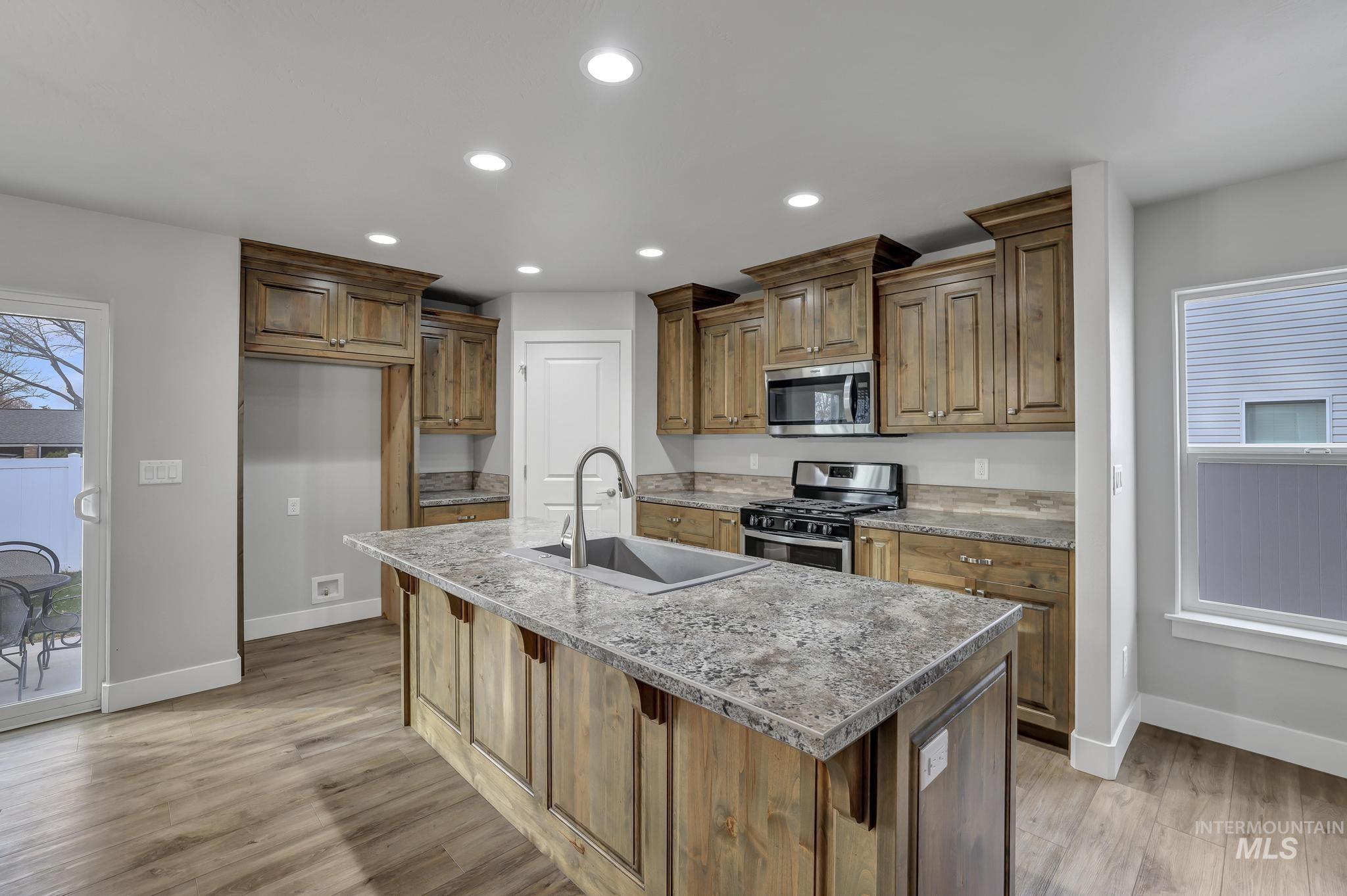 Kitchen featuring healthy amount of natural light, appliances with stainless steel finishes, recessed lighting, a kitchen island with sink, and light stone countertops
