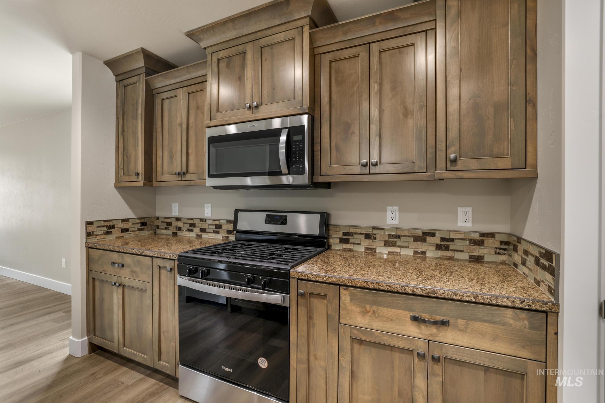 Kitchen featuring appliances with stainless steel finishes, light stone counters, brown cabinets, light wood finished floors, and tasteful backsplash