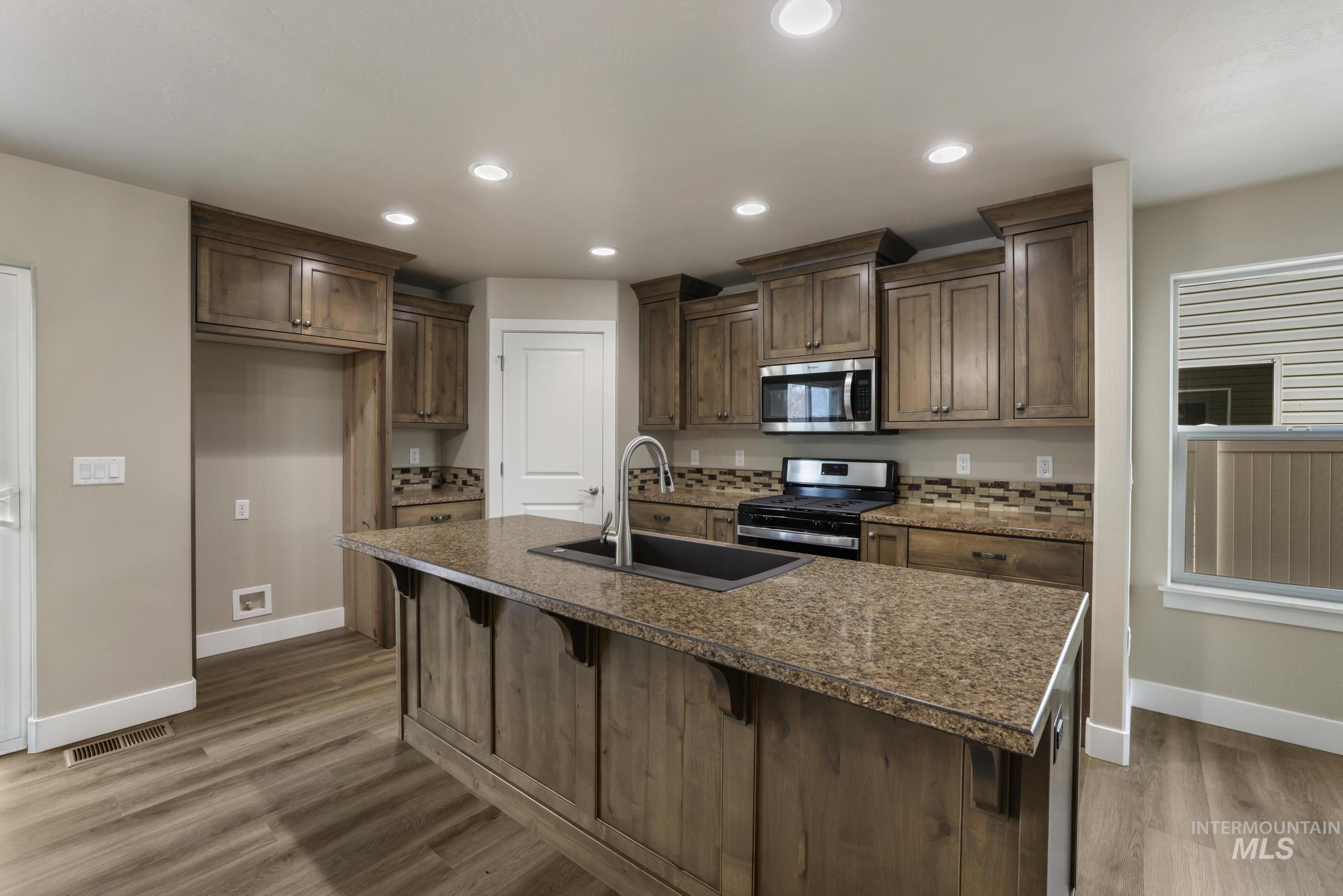 Kitchen with stainless steel appliances, a kitchen breakfast bar, a kitchen island with sink, recessed lighting, and light wood-type flooring