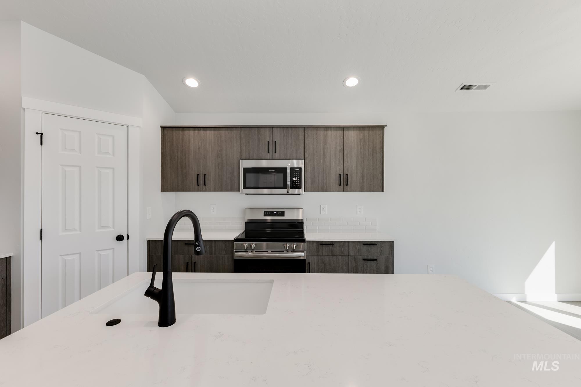 Kitchen featuring appliances with stainless steel finishes, light stone countertops, modern cabinets, dark brown cabinetry, and recessed lighting