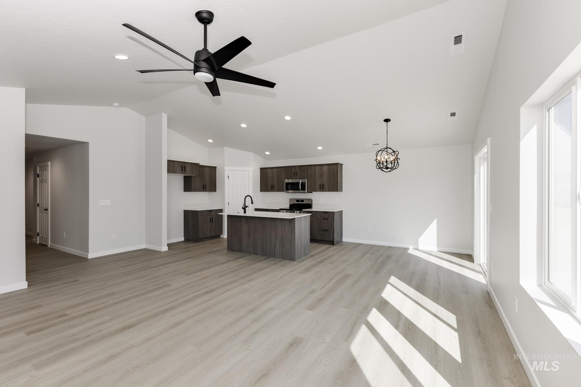 Kitchen featuring open floor plan, light countertops, light wood-style flooring, ceiling fan, and a kitchen island with sink