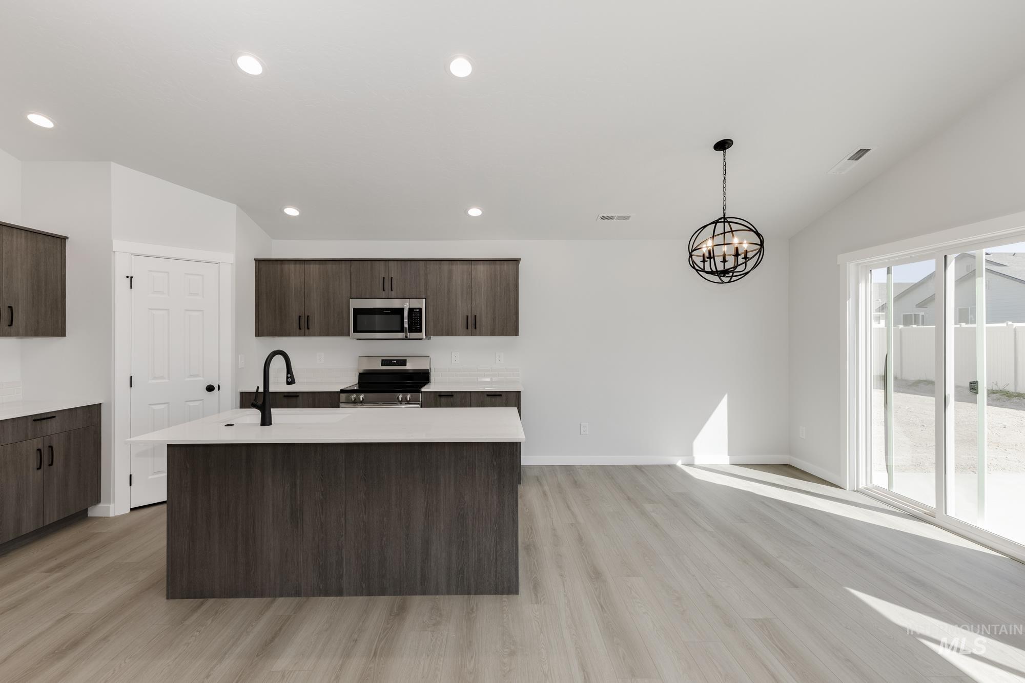 Kitchen with decorative light fixtures, an island with sink, dark brown cabinets, appliances with stainless steel finishes, and light wood-type flooring