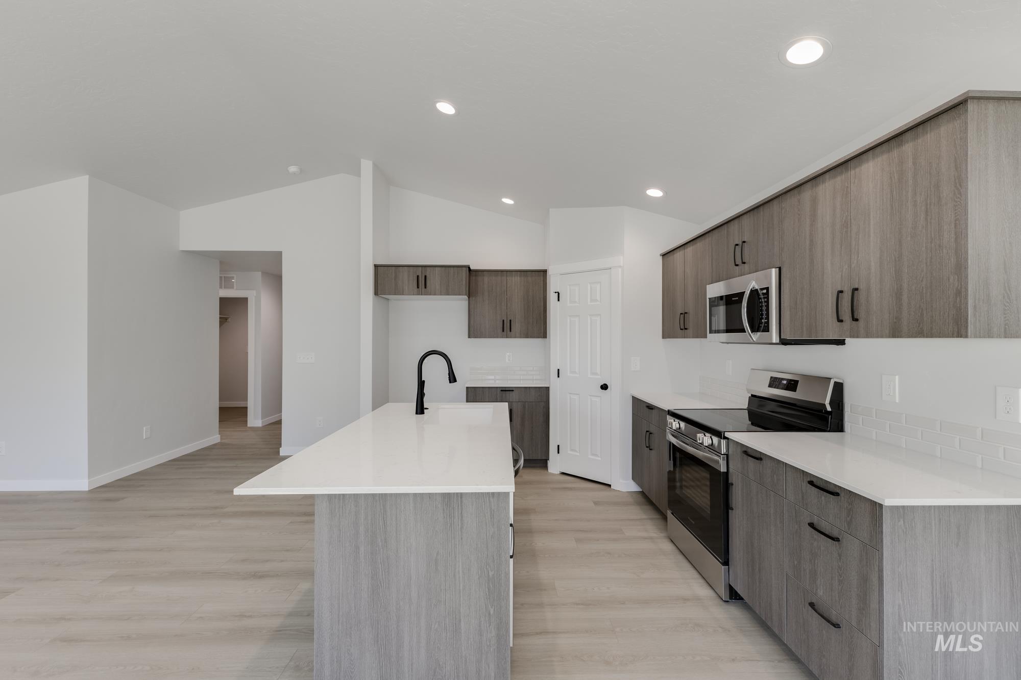 Kitchen featuring appliances with stainless steel finishes, modern cabinets, a center island with sink, light wood-style flooring, and vaulted ceiling