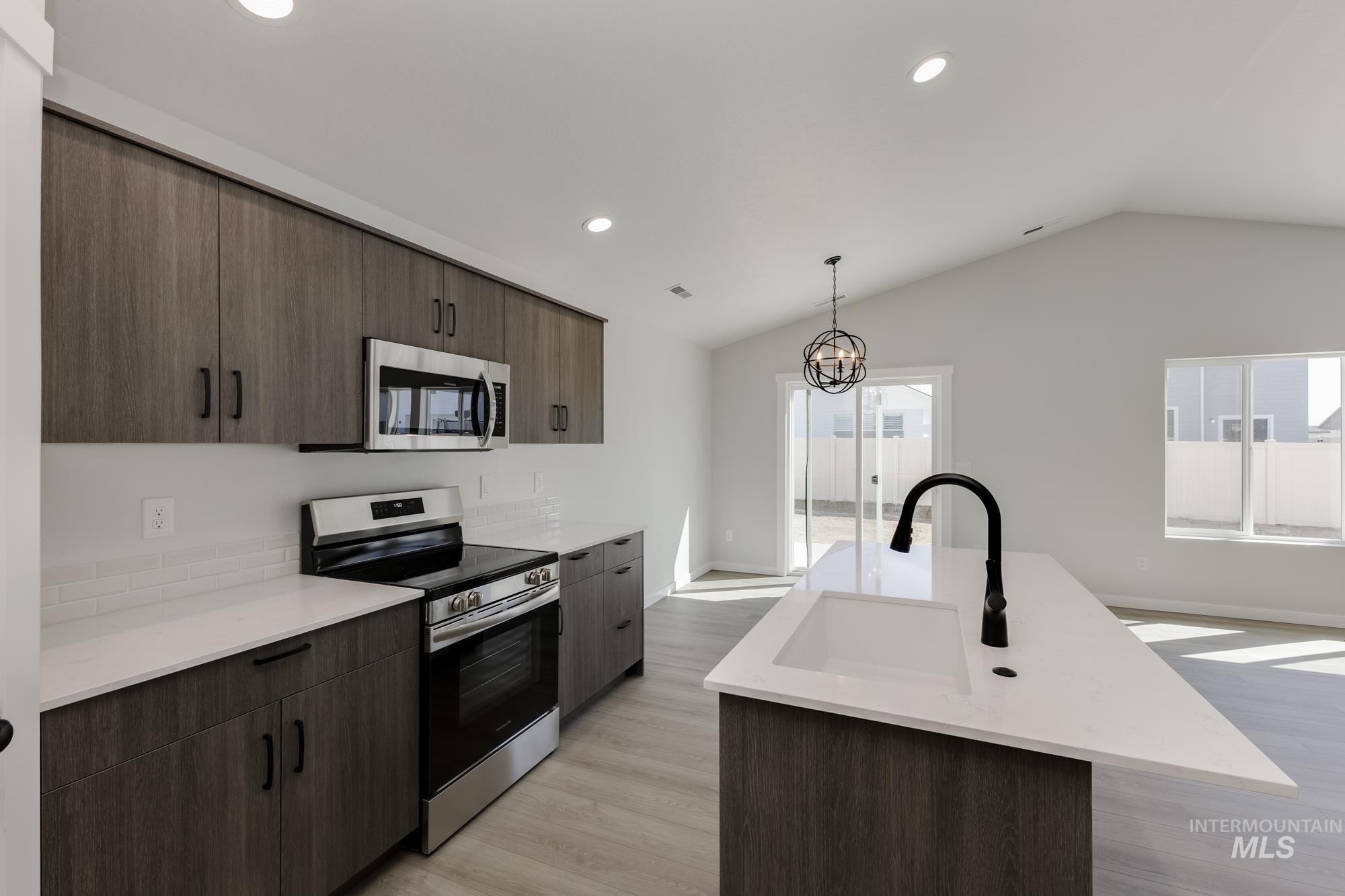 Kitchen with appliances with stainless steel finishes, light wood-type flooring, dark brown cabinetry, an island with sink, and recessed lighting