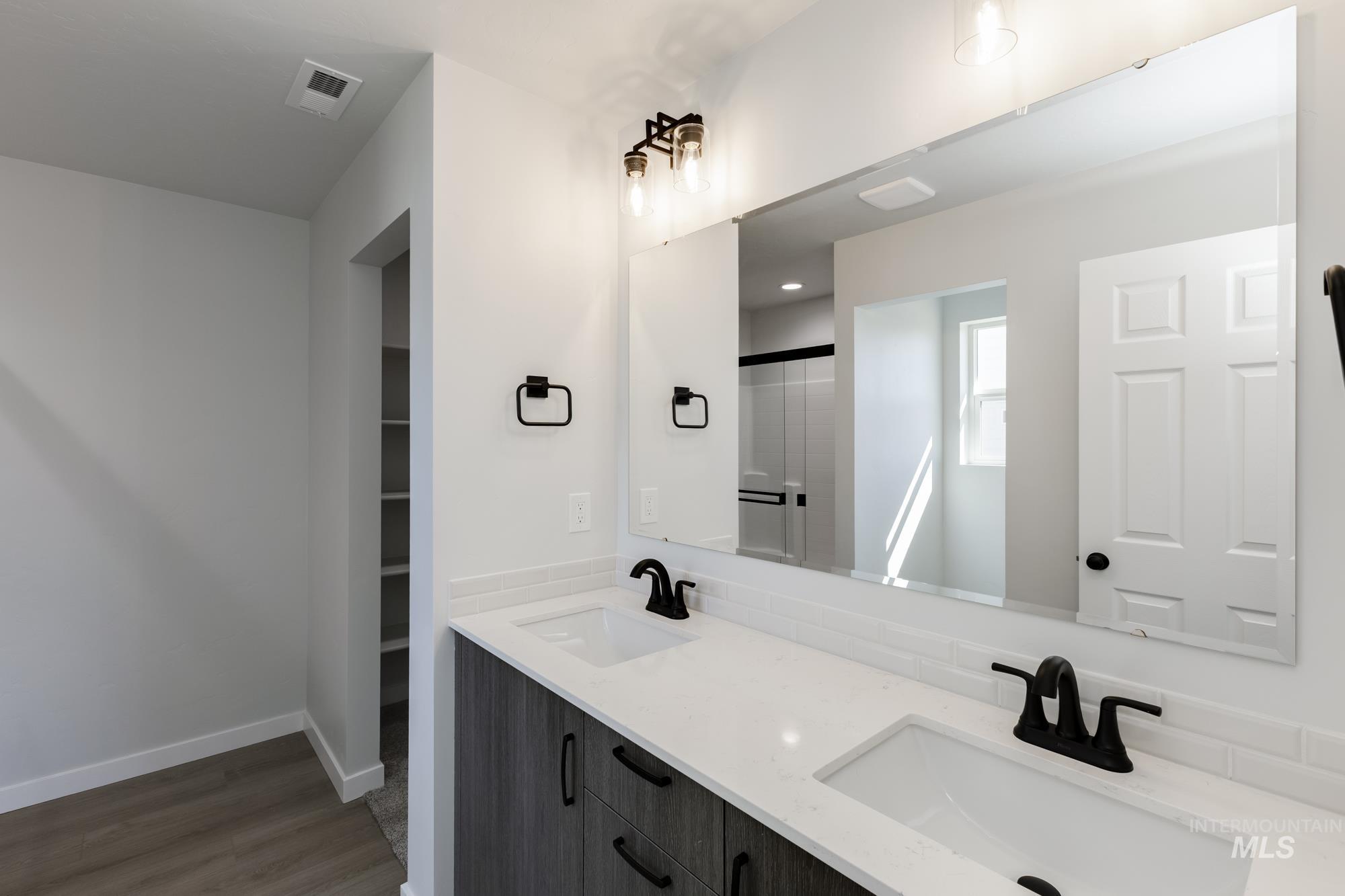 Bathroom with double vanity, dark wood-type flooring, a walk in closet, and a shower with shower door