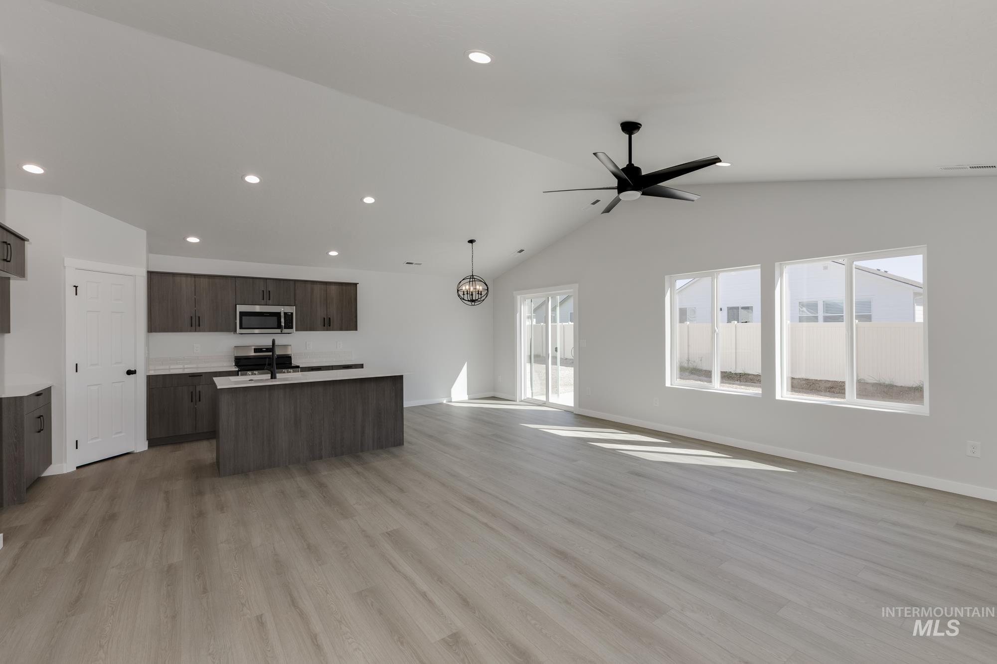 Kitchen featuring open floor plan, a kitchen island with sink, light wood finished floors, lofted ceiling, and ceiling fan