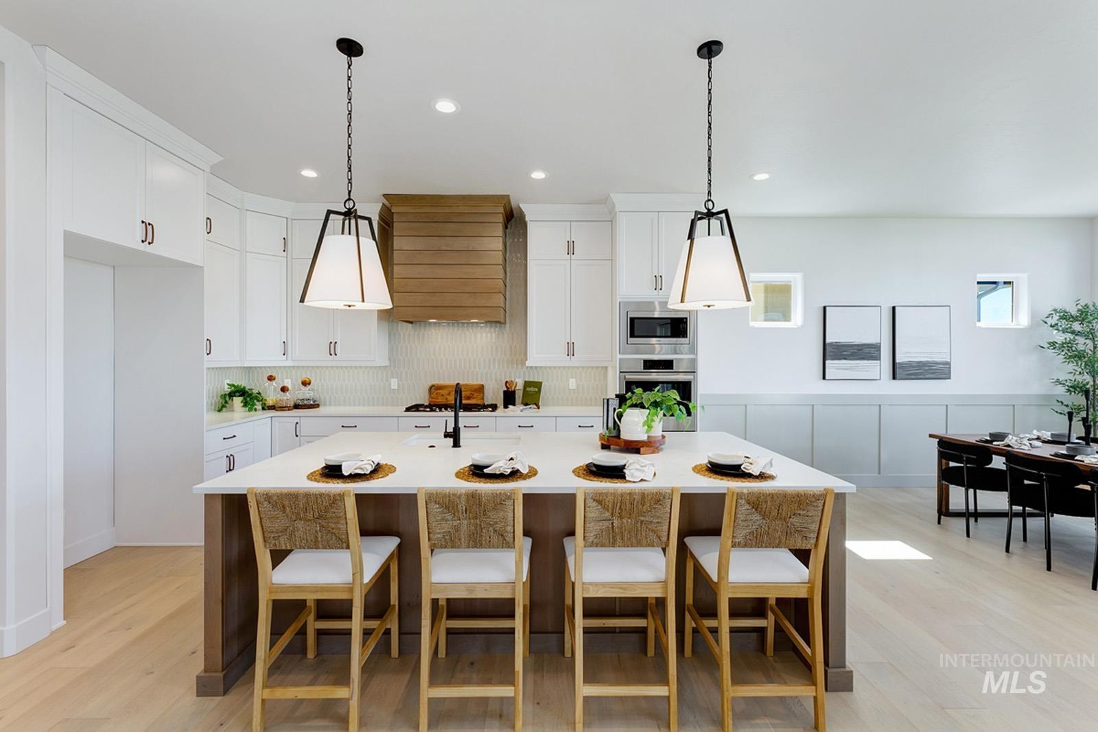Kitchen featuring pendant lighting, a breakfast bar, white cabinets, a center island with sink, and light wood-style floors