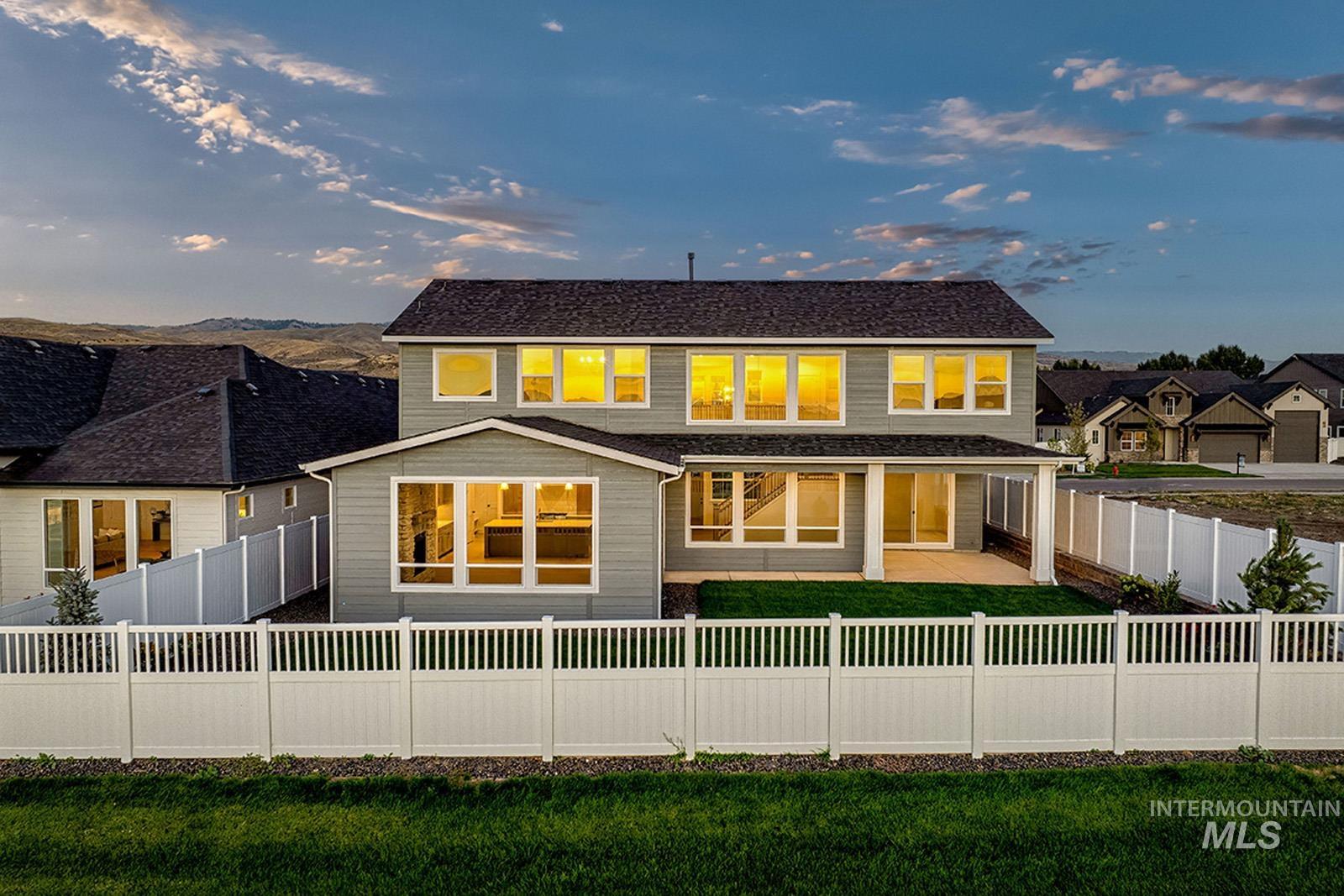 Back of house at dusk featuring a fenced backyard, a patio area, a residential view, and a shingled roof