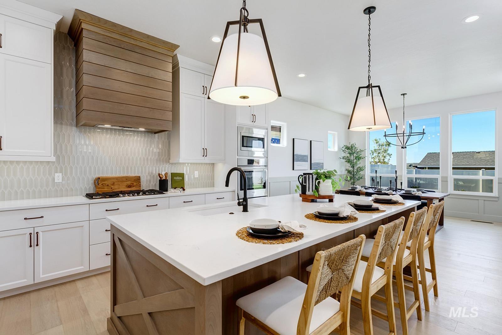 Kitchen with dual tone cabinetry, decorative backsplash, an island with sink, light wood finished floors, and decorative light fixtures