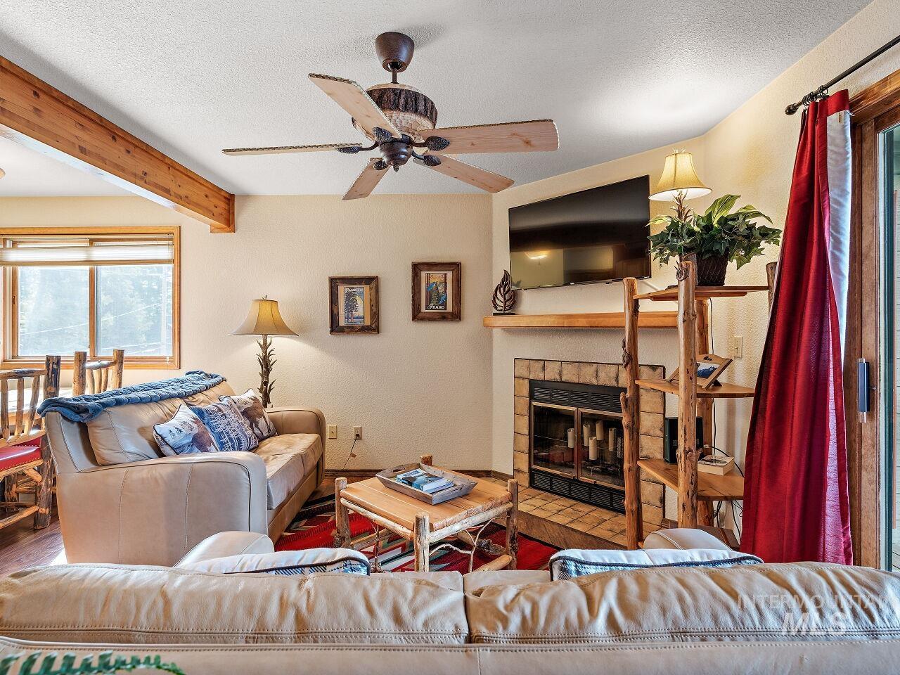 Living room with ceiling fan, a tile fireplace, a textured ceiling, wood finished floors, and beam ceiling