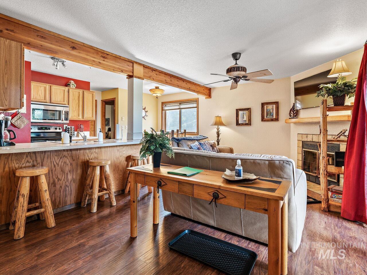 Living room with wood finished floors, ceiling fan, beam ceiling, a textured ceiling, and a tiled fireplace