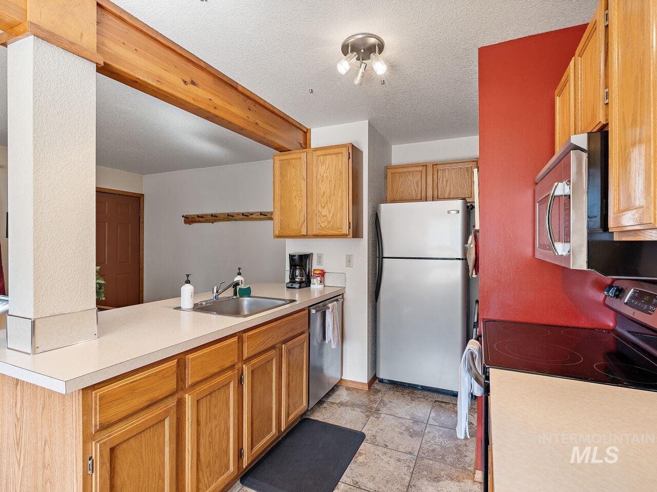 Kitchen featuring appliances with stainless steel finishes, light countertops, beamed ceiling, and a textured ceiling