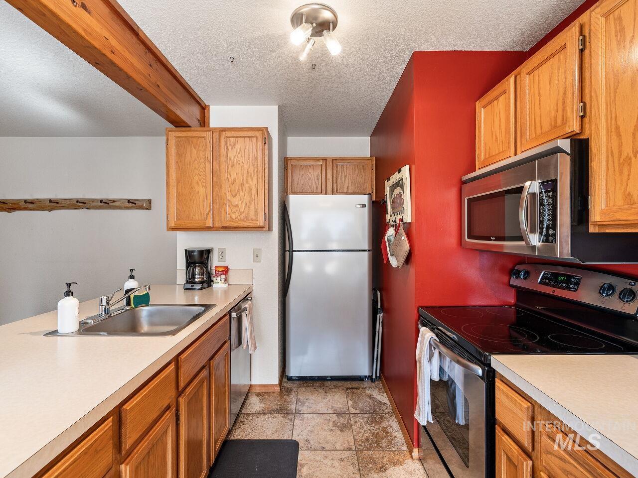 Kitchen with stainless steel appliances, light countertops, brown cabinetry, and a textured ceiling