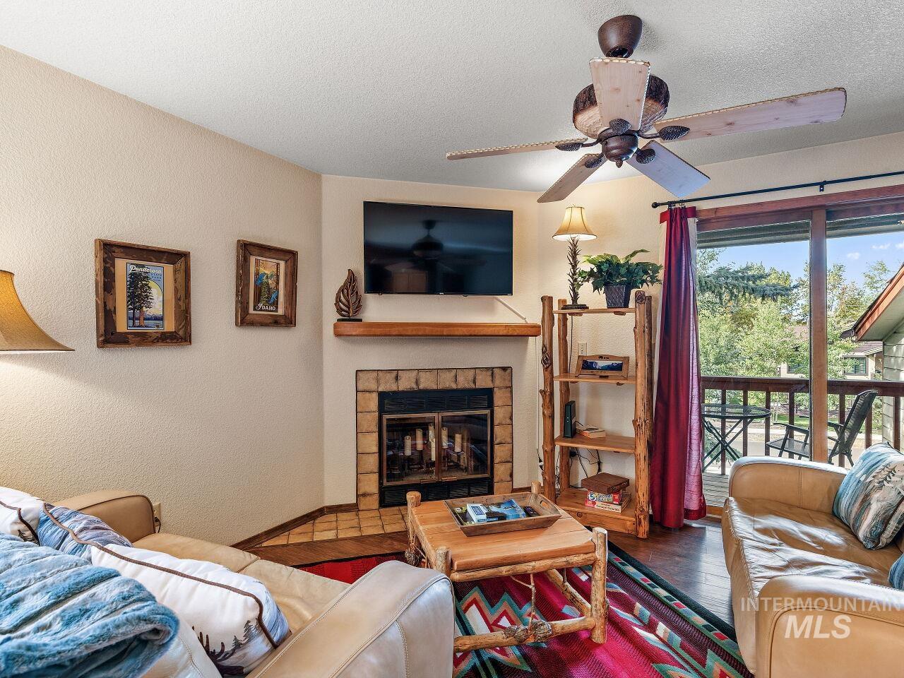 Living room featuring a ceiling fan, wood finished floors, a glass covered fireplace, a textured ceiling, and a textured wall