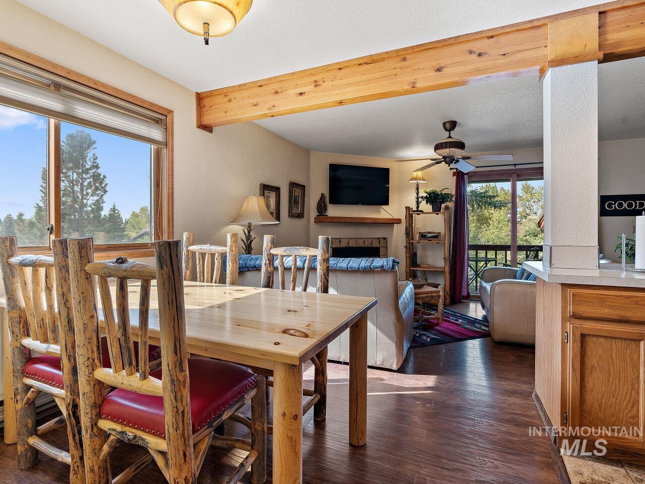 Dining room featuring ceiling fan, dark wood-style flooring, a fireplace, and beamed ceiling