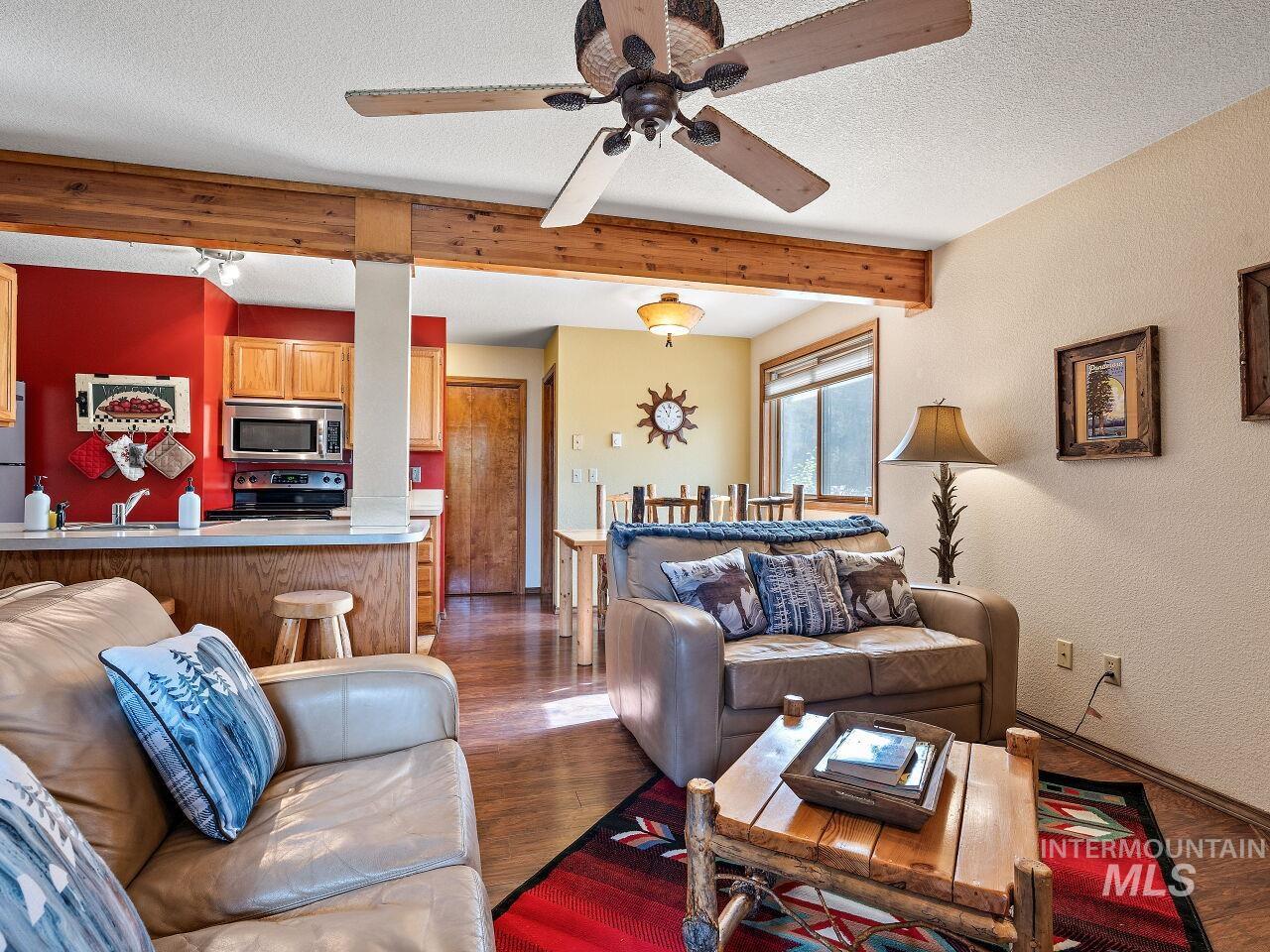 Living area with a ceiling fan, beam ceiling, wood finished floors, a textured ceiling, and a textured wall