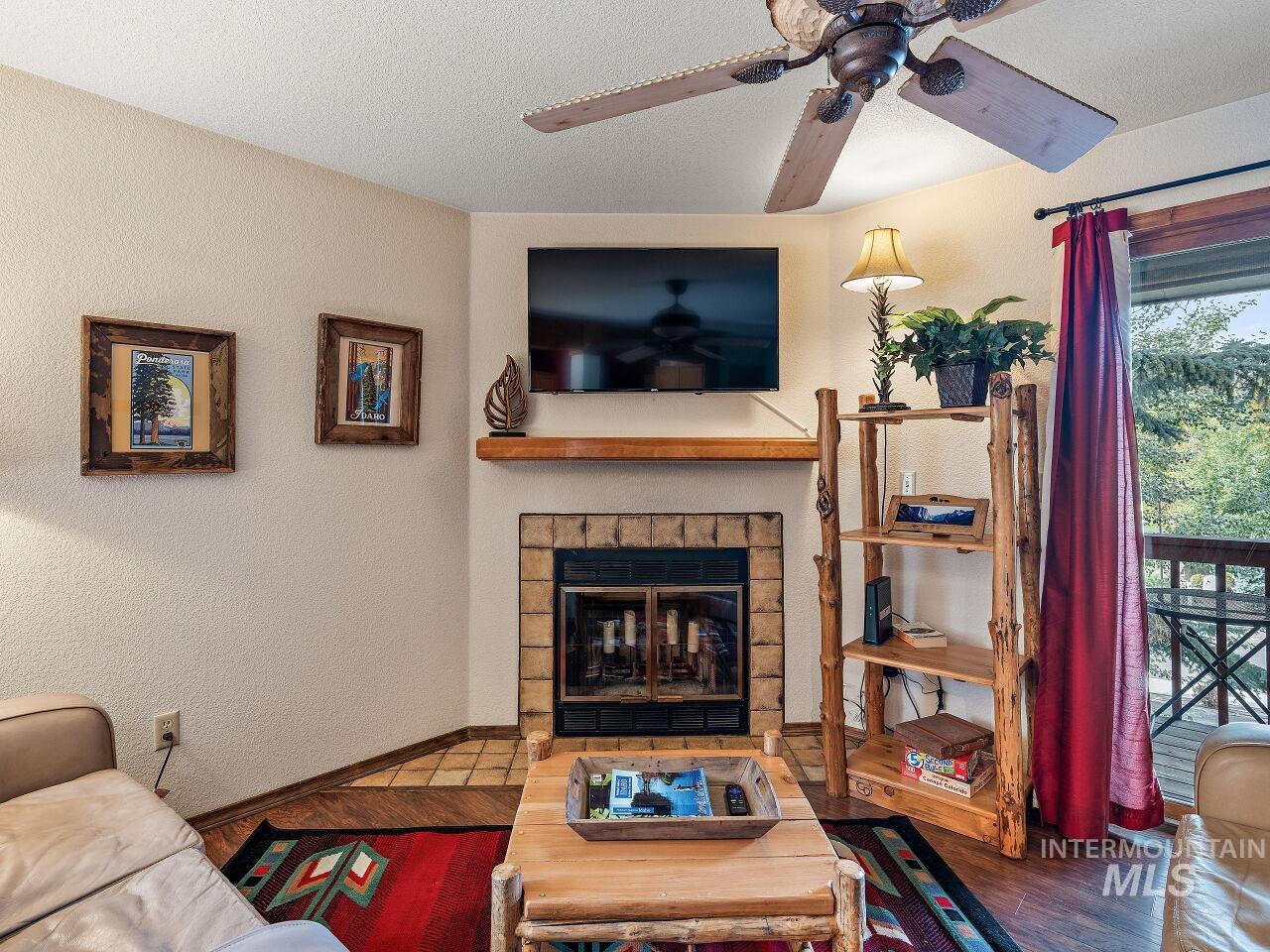 Living room with a ceiling fan, wood finished floors, a brick fireplace, and a textured ceiling