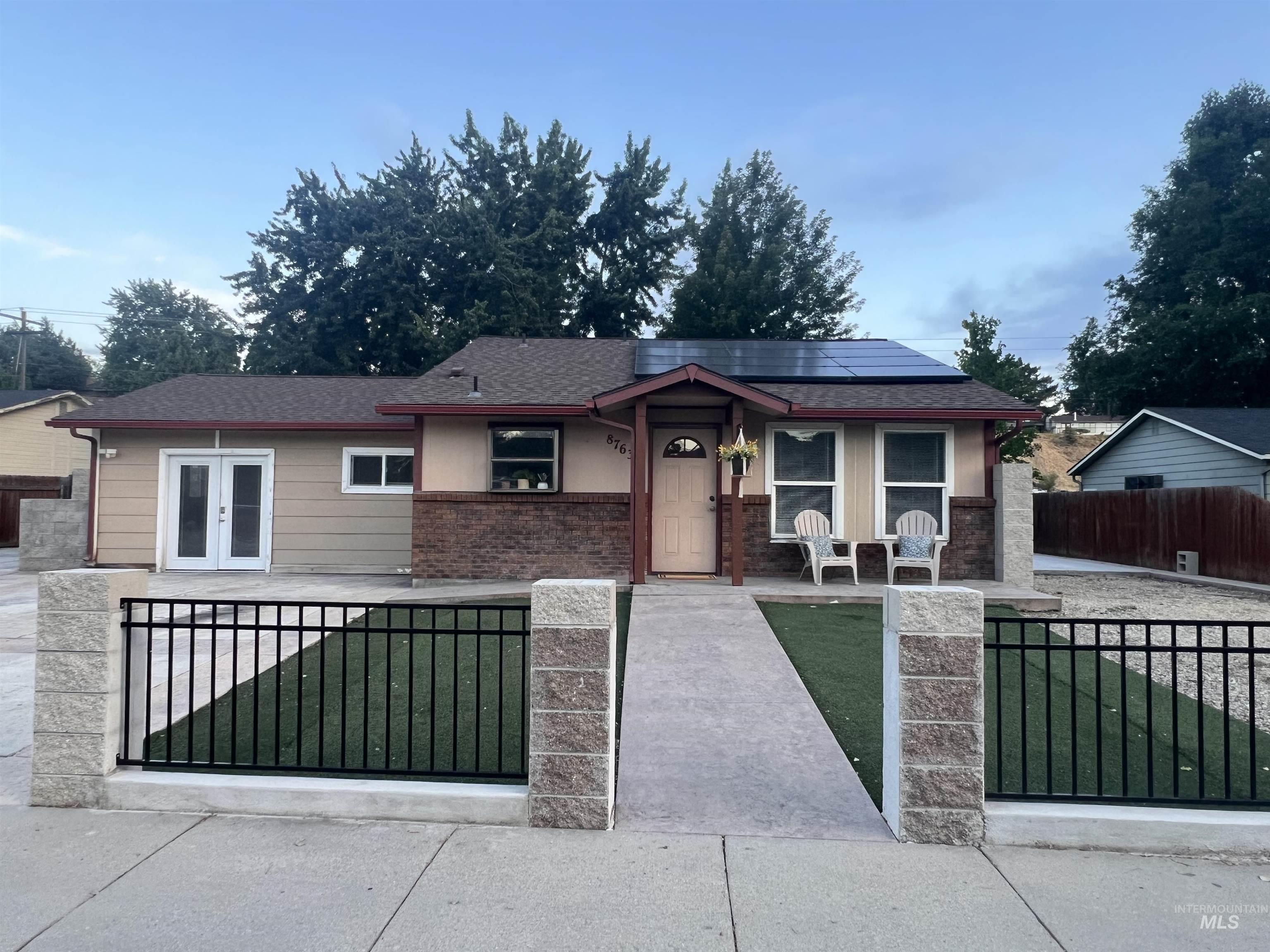 Contemporary home exterior featuring solar panels, a brown shingle roof, and a two-tone facade with a light-colored upper section and a brick-finish lower section