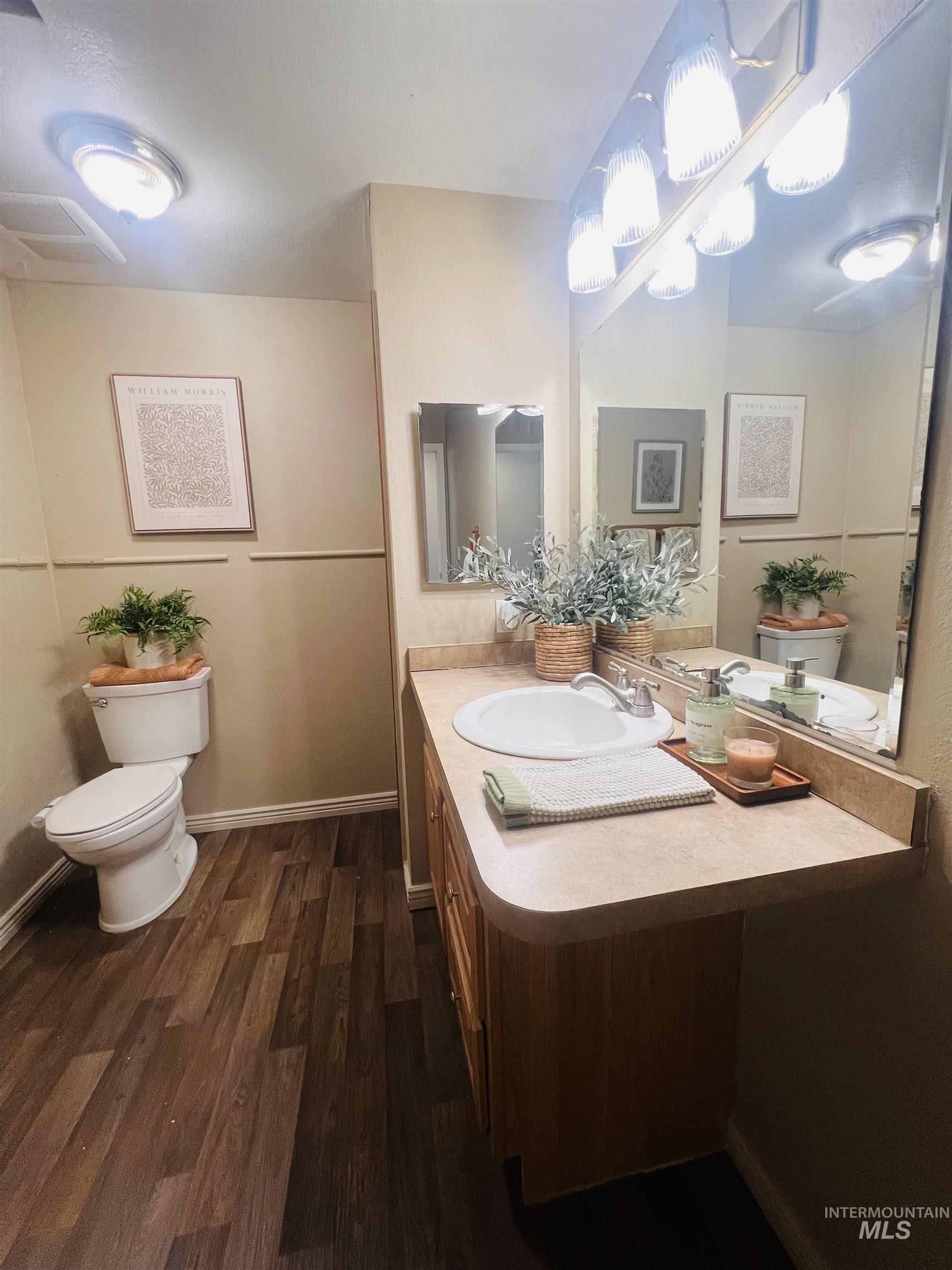 Bathroom featuring wood-finish flooring, a single vanity with a laminate countertop, a white drop-in sink, and a framed mirror