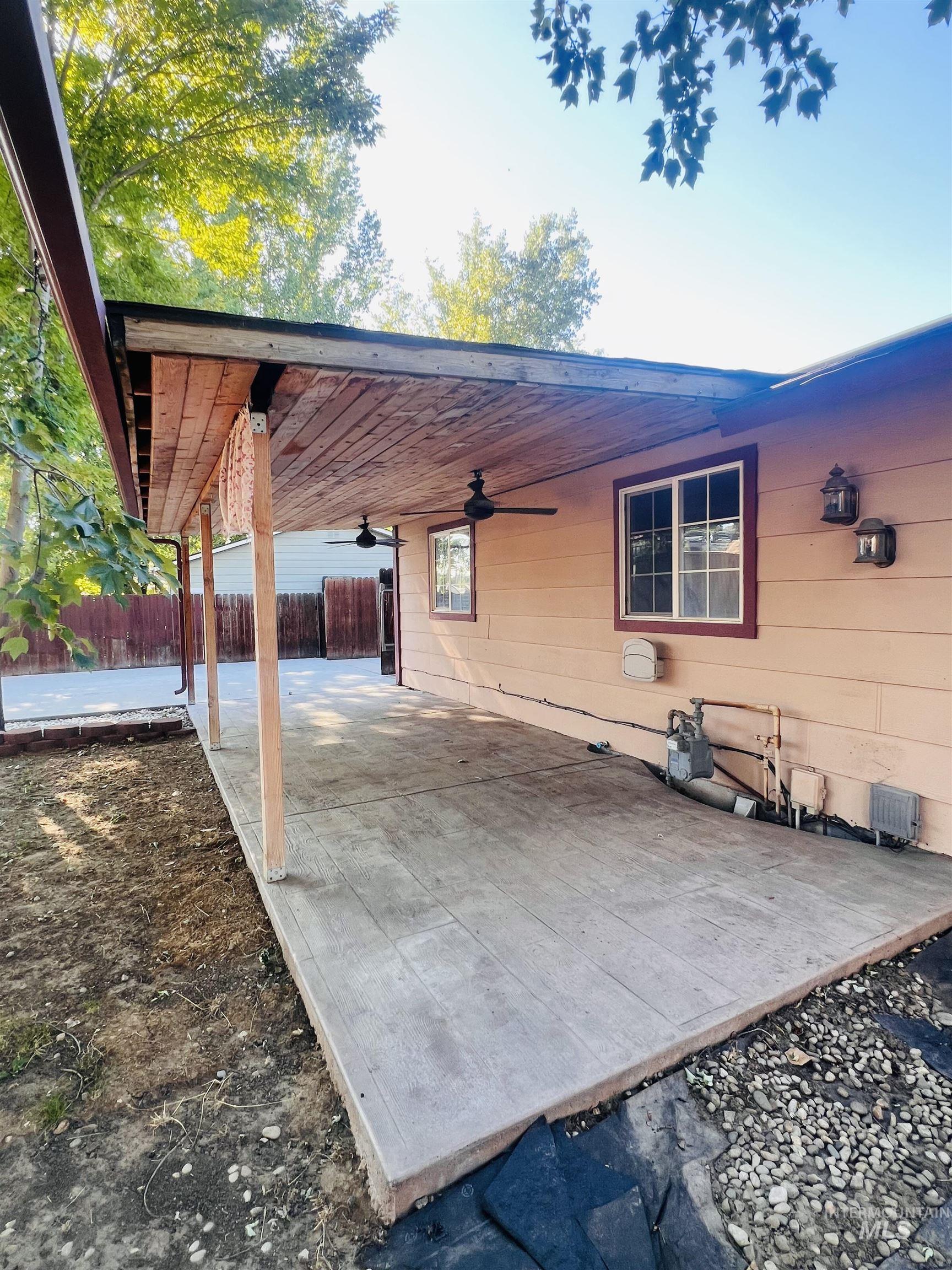 Expansive covered patio featuring a wood-finish ceiling, two ceiling fans, stamped concrete flooring to look like wood planks, and wall-mounted exterior lighting fixtures