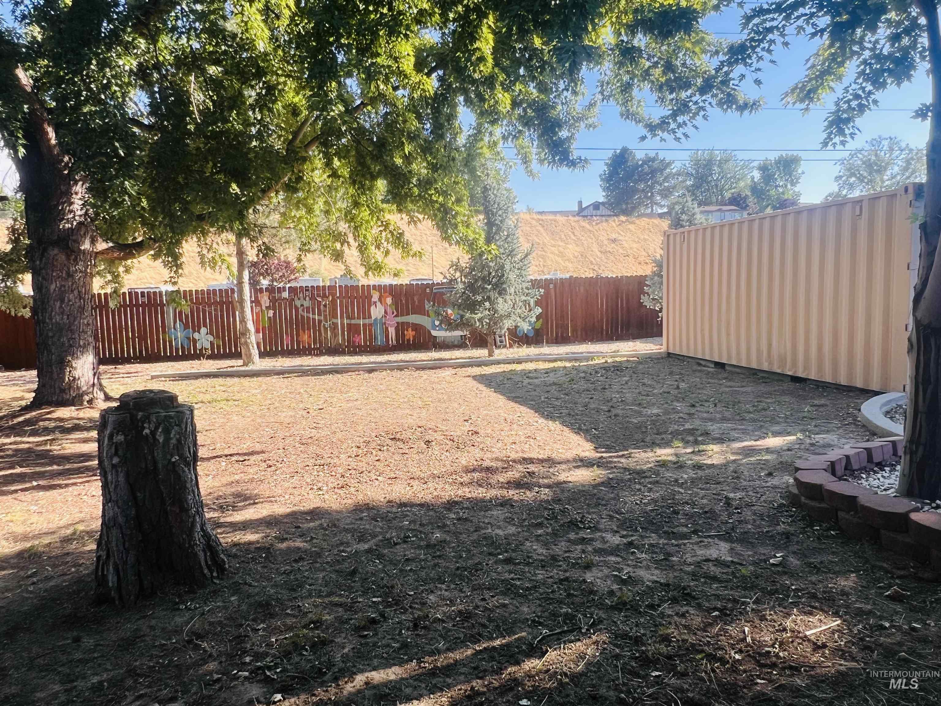 Expansive outdoor space featuring a wood-panel fence, mature trees, and a large storage container